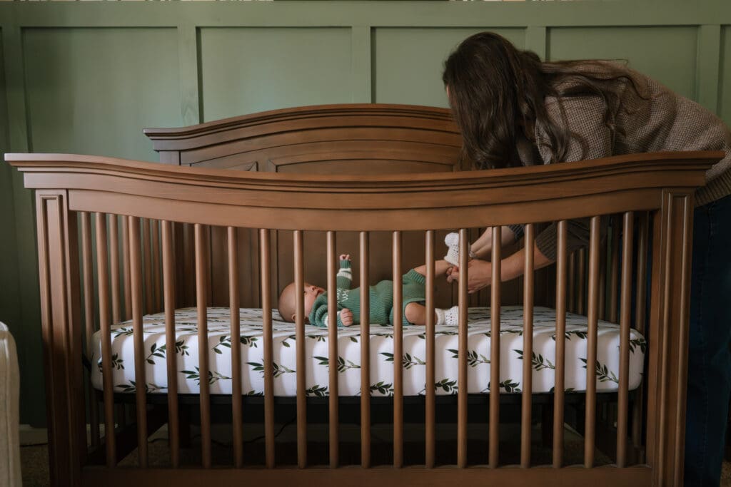 mom changing newborns socks in crib during in home family session in chattanooga, tn