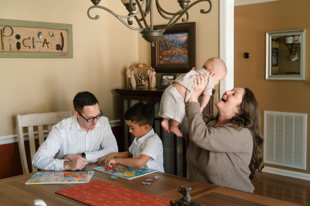 Playful family moment with mom holding baby up near the dining table during a relaxed in-home family photography session.