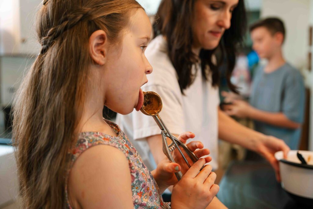 little girl licking spoon while baking in kichen with mom
