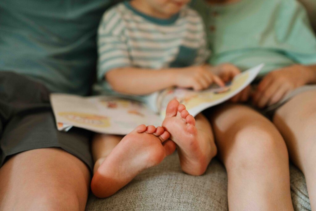 little boy reading book with siblings in home