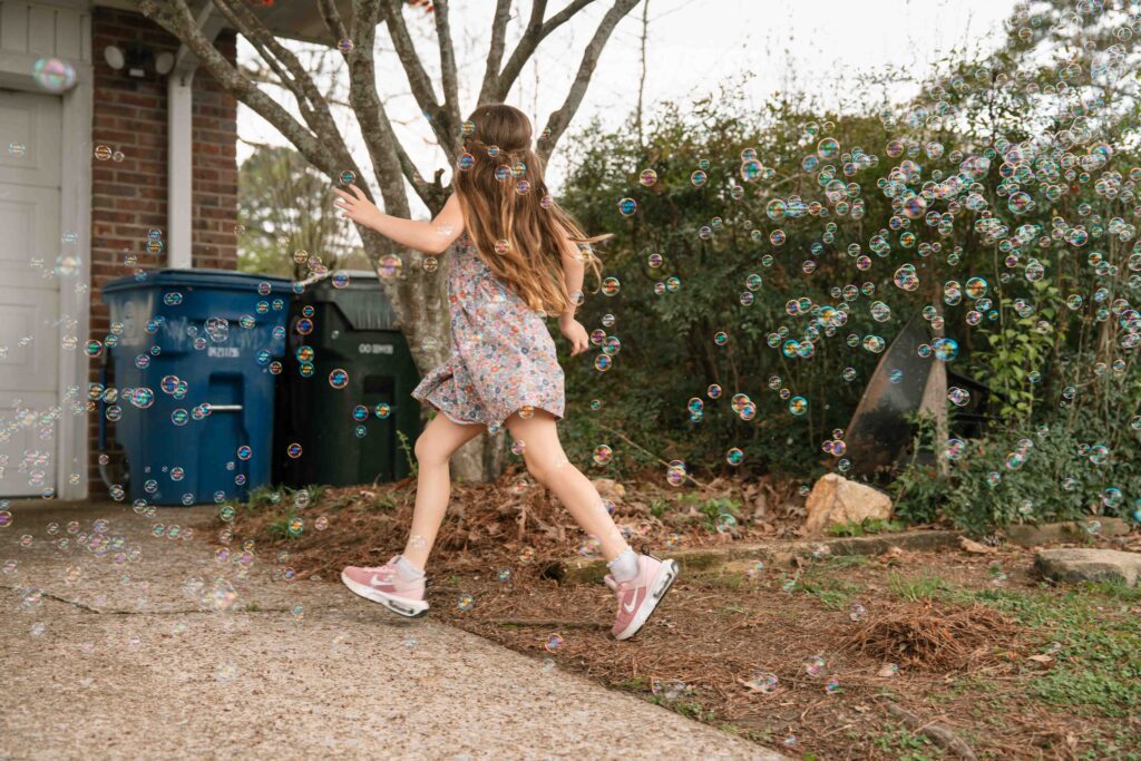 little girl playing in bubbles outside of home