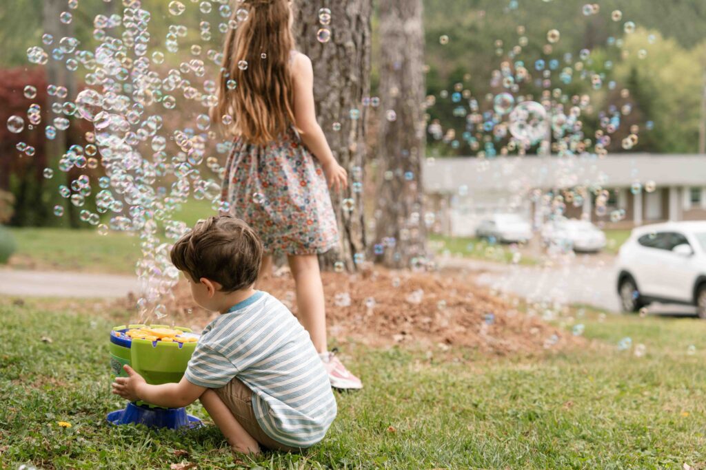 siblings playing in bubbles in front yard