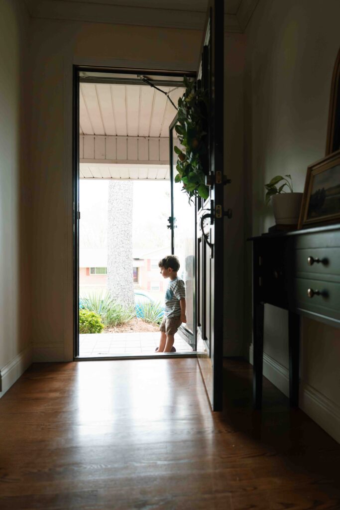 little boy looking out front door of home
