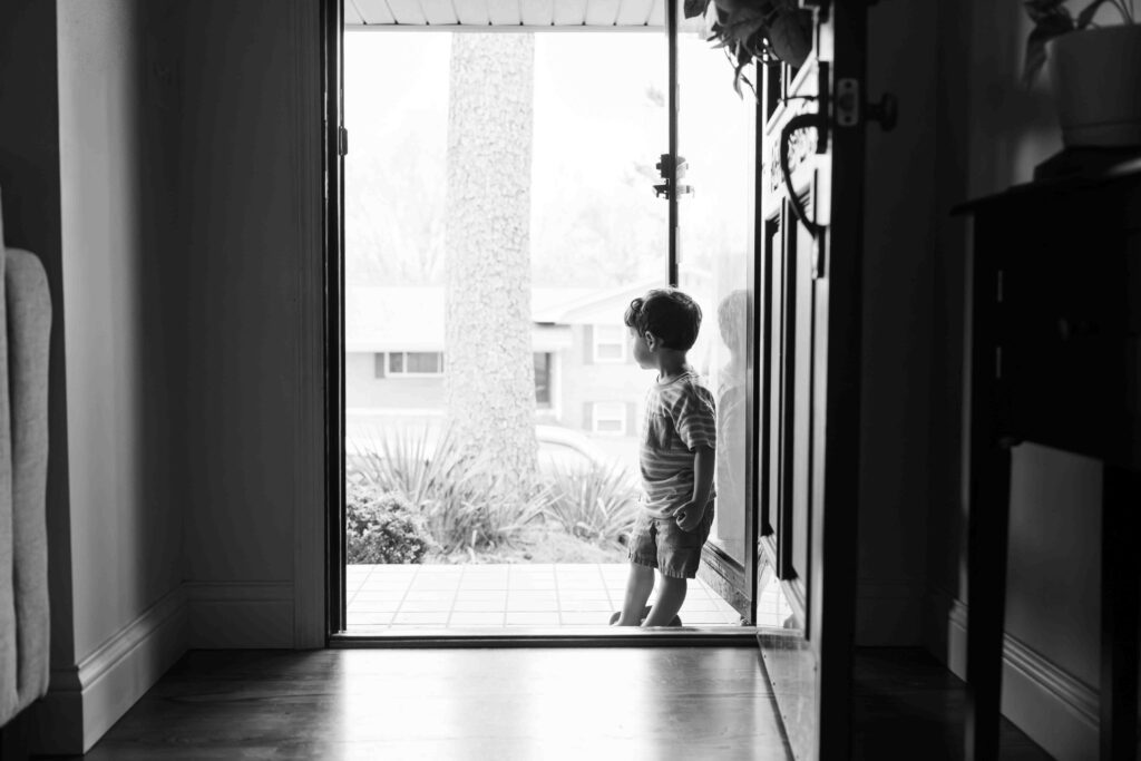 picture of little boy looking out front door of home.