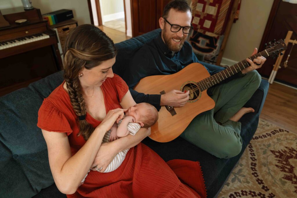 dad playing guitar as mom and newborn listen