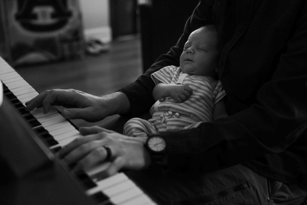 picture of dad playing piano while he holds newborn