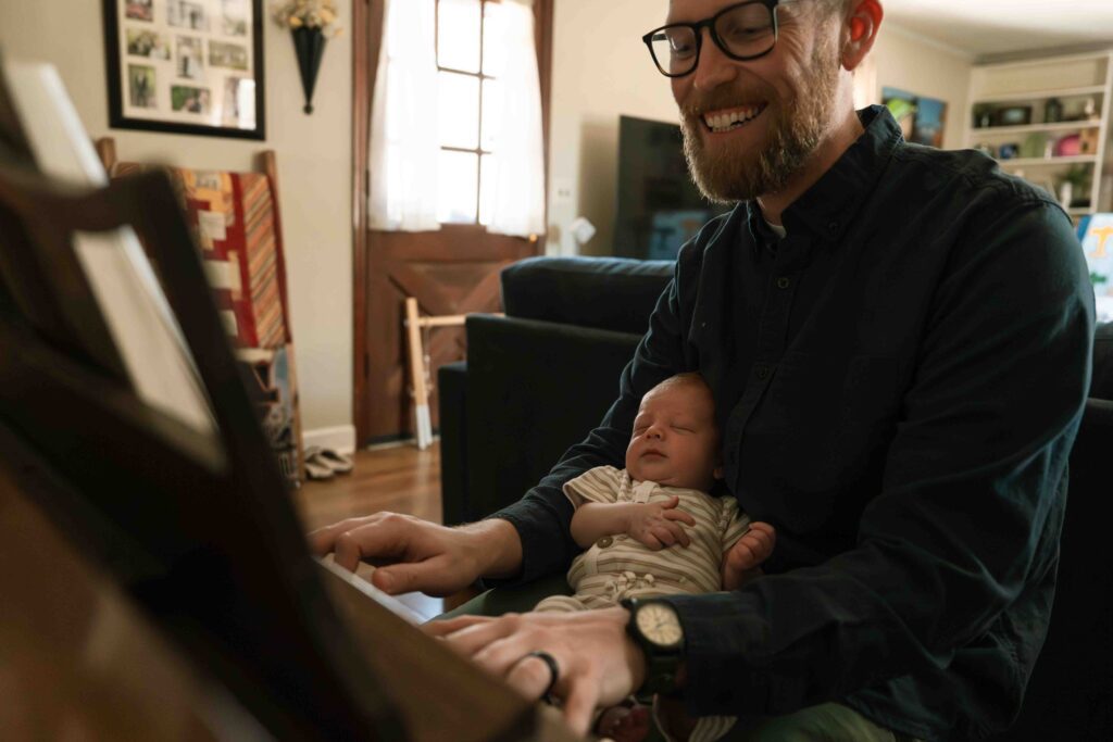 dad playing piano holding newborn baby boy