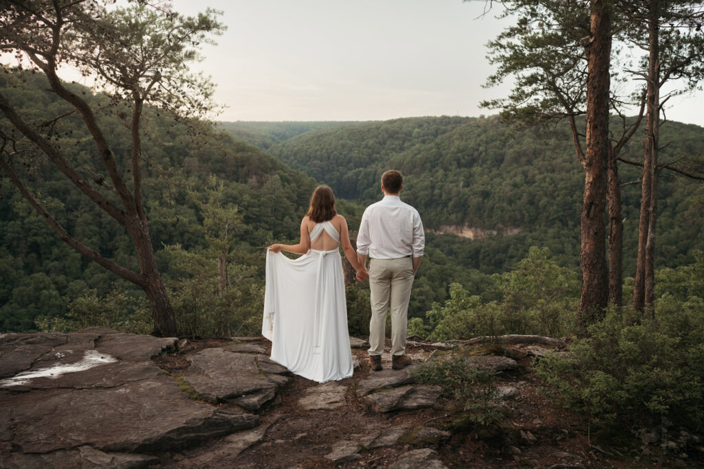 Couple holding hands on a rocky overlook facing a forested Tennessee mountain valley during their elopement