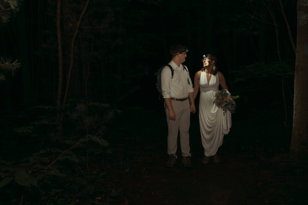 Couple wearing headlamps and hiking backpack walking hand in hand through dark forest during their Cumberland Trail elopement in Tennessee