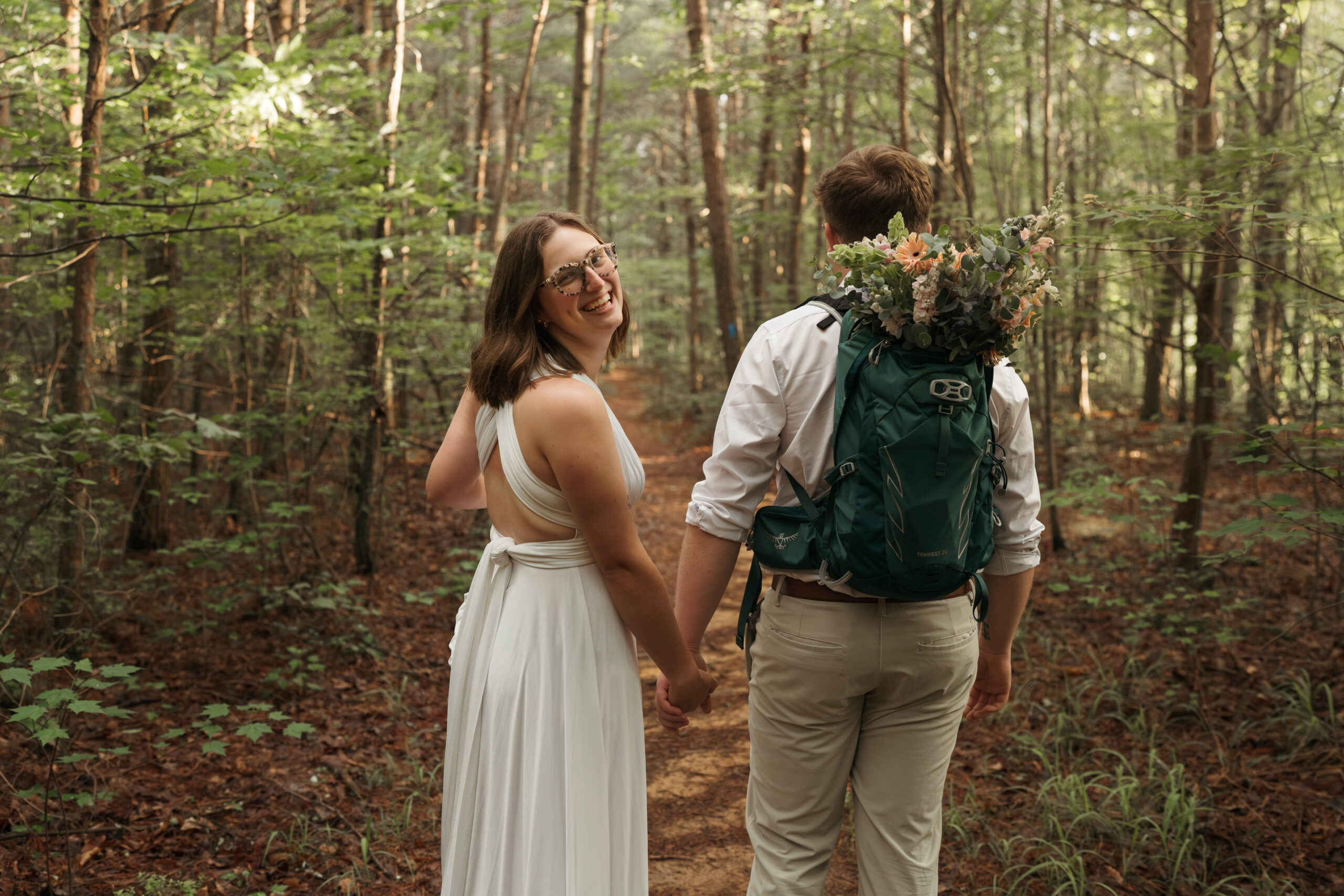 Bride laughing over her shoulder while holding hands with groom on a wooded elopement trail
