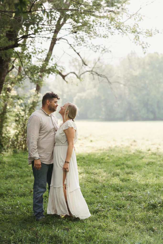 Couple smiling and embracing under a tree in a misty green field during their elopement