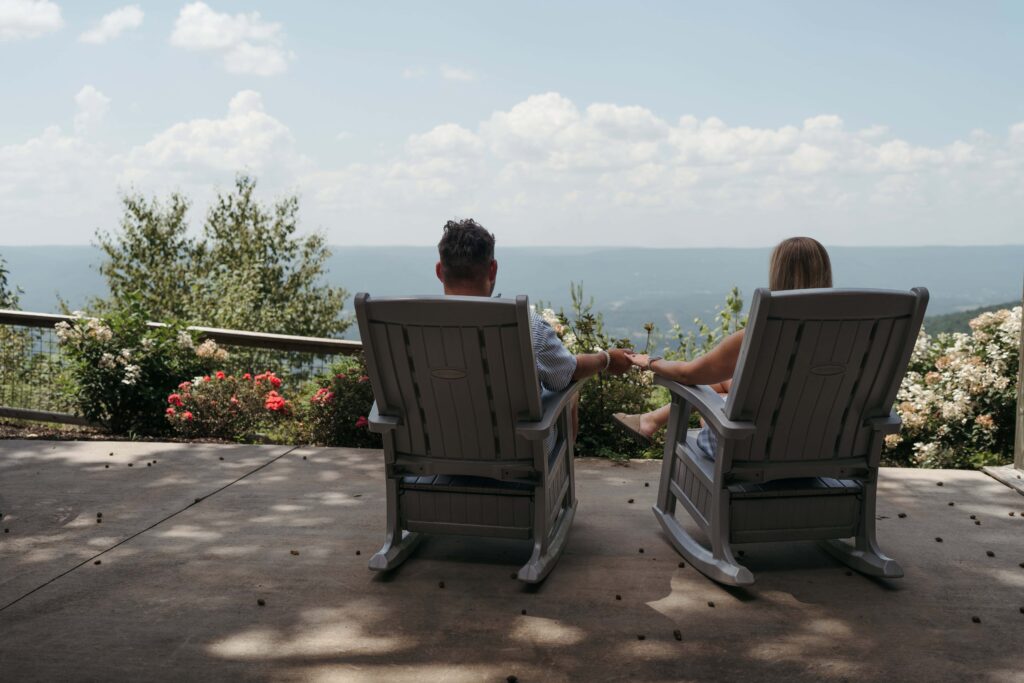 Couple holding hands in rocking chairs on a porch overlooking the Tennessee mountains.