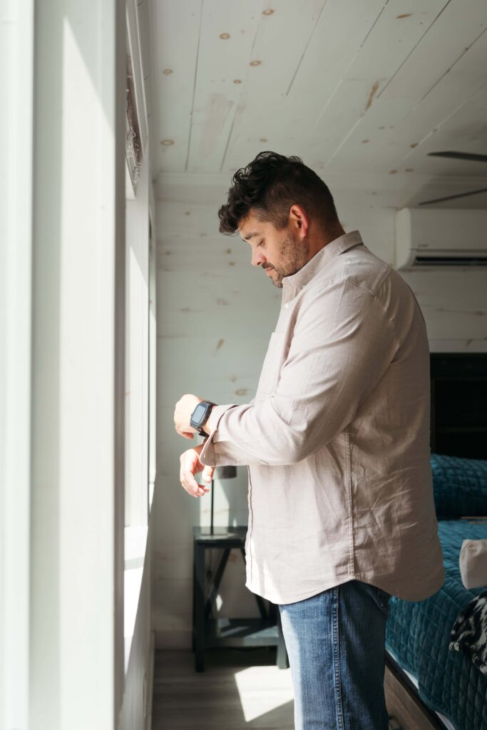 Groom checking his watch while getting ready in a sunlit cabin bedroom before the ceremony