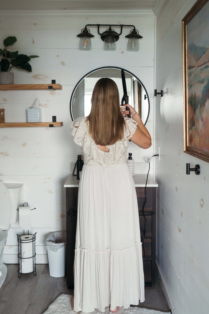 Bride curling her hair in a bathroom mirror while getting ready for her elopement